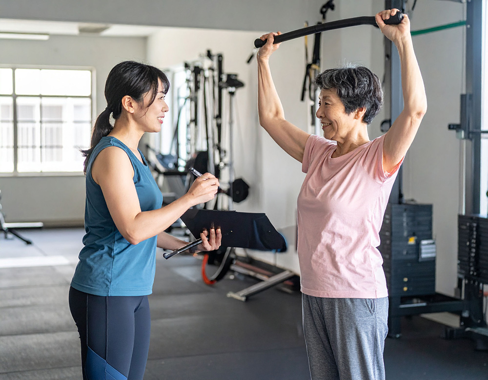 高齢女性が運動し、トレーナーの女性が付き添っている